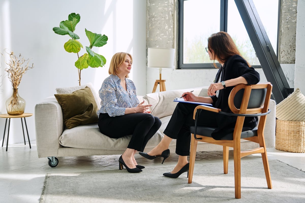 Mental therapy session, middle aged businesswoman patient talking to professional psychologist psychotherapist mental therapist, sitting together on couch. Psychology psychotherapy counseling concept